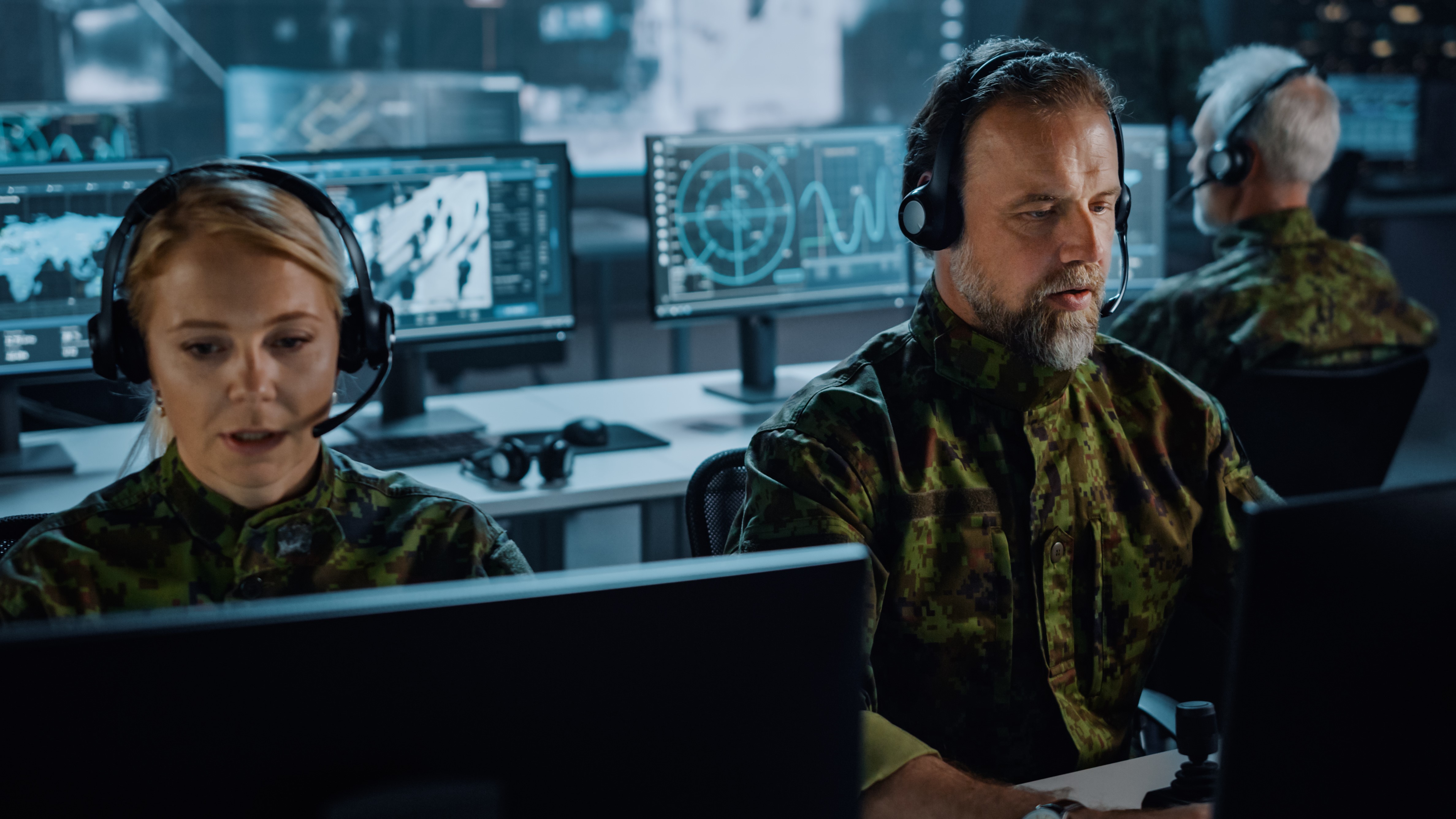 Two members of armed forces - a man and a woman - wearing uniform are sitting working at screens