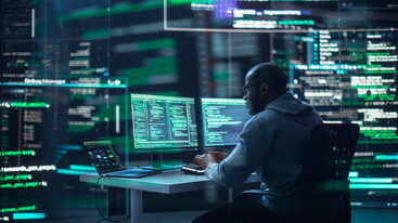 man sitting at screens looking at computer code