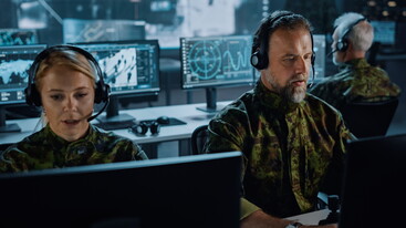 Two members of armed forces - a man and a woman - wearing uniform are sitting working at screens