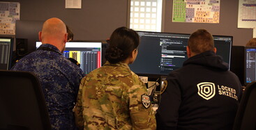 Back view of two men and a woman in army camouflage clothing sitting in front of screens