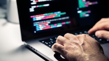 Close-up of hands typing on laptop with blurred coloured code on the screen